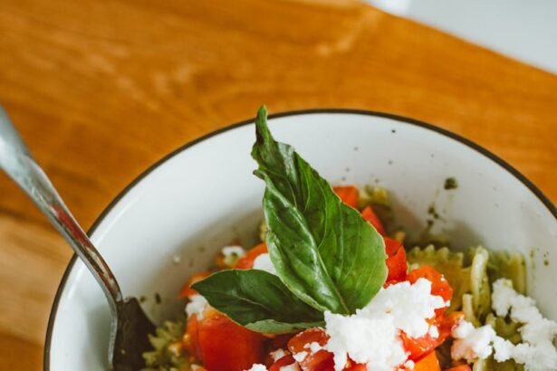Delicious pesto pasta topped with fresh tomatoes, feta cheese, and basil in a white bowl.