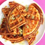 Plate of crispy waffles with bacon, cheddar cheese, and scallions.
