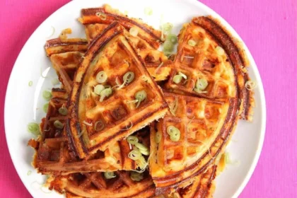 Plate of crispy waffles with bacon, cheddar cheese, and scallions.