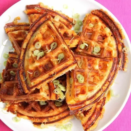 Plate of crispy waffles with bacon, cheddar cheese, and scallions.
