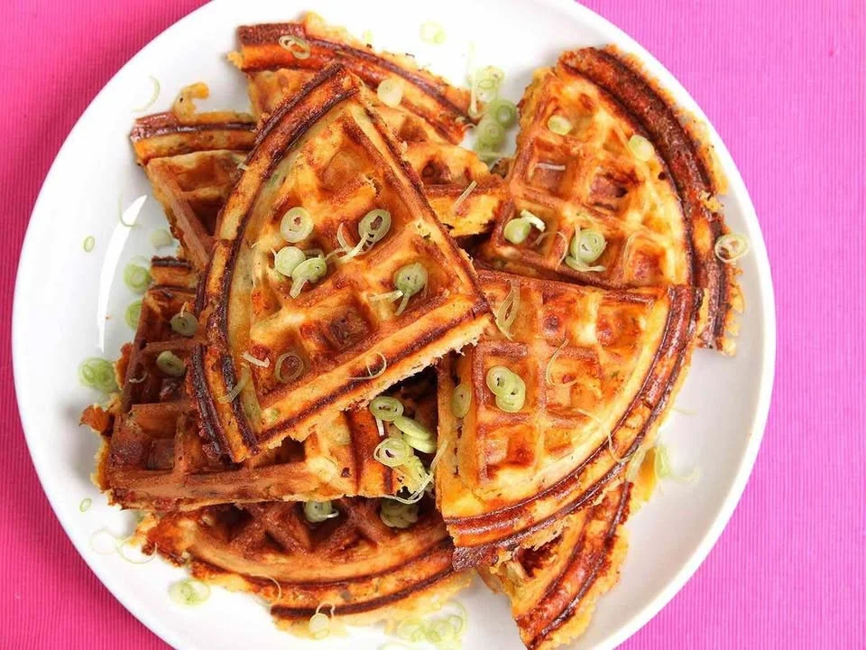 Plate of crispy waffles with bacon, cheddar cheese, and scallions.