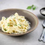 Delicious plate of Fettuccine Alfredo topped with parsley and grated cheese.