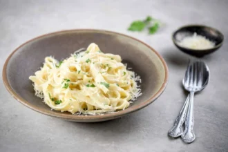 Delicious plate of Fettuccine Alfredo topped with parsley and grated cheese.