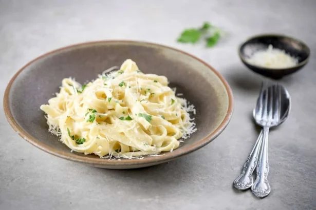Delicious plate of Fettuccine Alfredo topped with parsley and grated cheese.