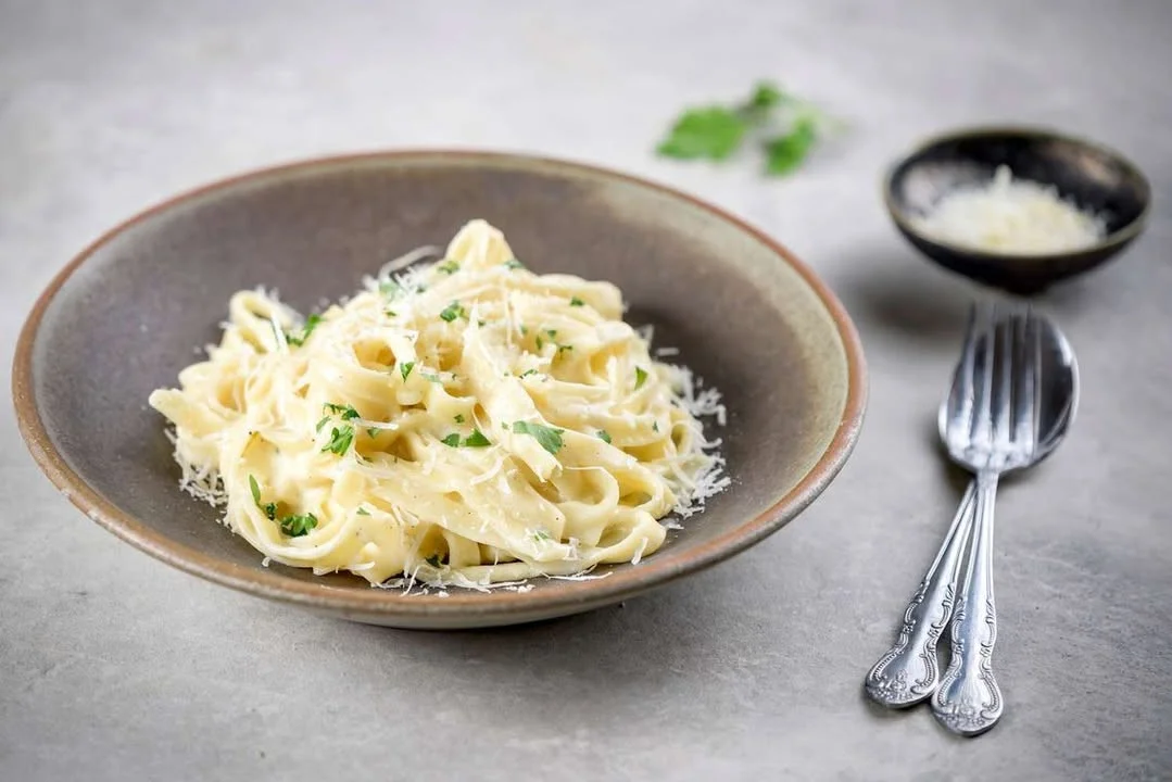 Delicious plate of Fettuccine Alfredo topped with parsley and grated cheese.