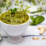 Homemade pesto sauce with fresh basil and pine nuts in a bowl.