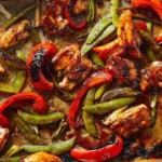 Sheet pan chicken thighs with snap peas and bell peppers cooking in the oven