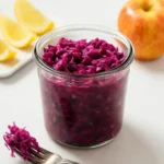 Homemade ginger apple sauerkraut in a glass jar with fresh apples and ginger