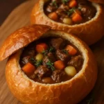 Hearty beef stew in a bread bowl, topped with herbs and fresh vegetables.